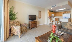 A living room with a sofa, two armchairs, a coffee table, a TV on a wooden stand, a kitchen area with a microwave, and a refrigerator. - Disney dreams apartment Amazing lake views! (Orlando)