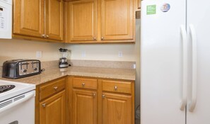 A kitchen with wooden cabinets, a white refrigerator, a toaster, and a blender. - Disney dreams apartment Amazing lake views! (Orlando)
