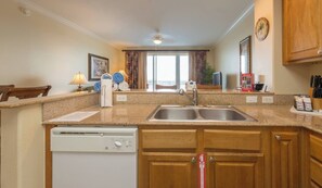 A kitchen with granite countertops, wooden cabinets, a dishwasher, a sink, and a window with curtains. - Disney dreams apartment Amazing lake views! (Orlando)