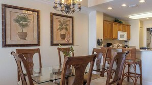 A dining area with a glass table and wooden chairs, a kitchen with wooden cabinets, and a chandelier. - Disney dreams Penthouse water view Mall restaurant (Orlando)