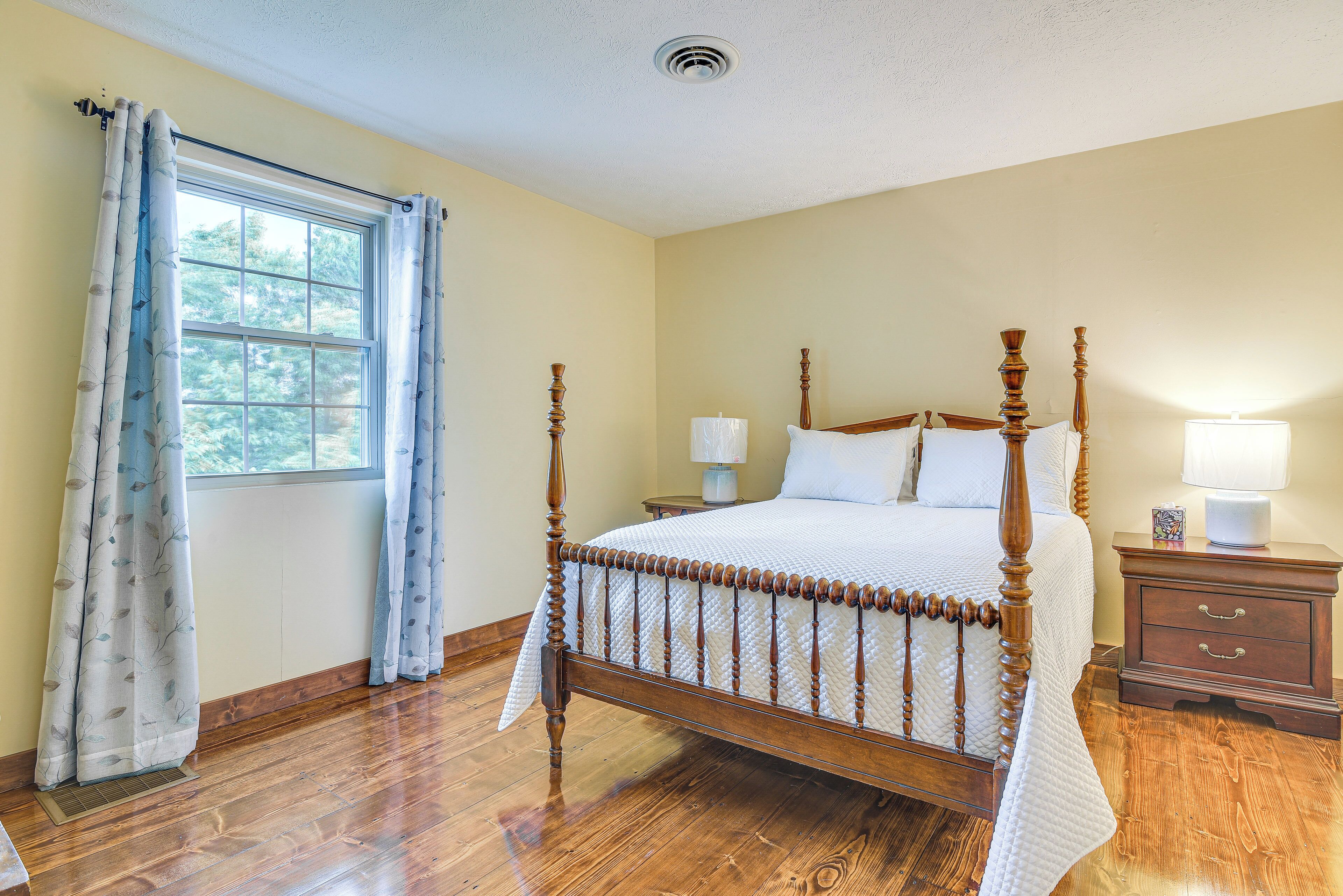 Une chambre à coucher avec un lit à baldaquin, une fenêtre avec des rideaux, une table de chevet avec une lampe et une commode en bois.