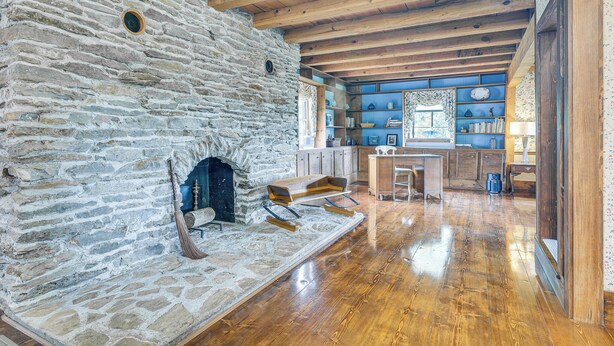 Chimenea de piedra, vigas de madera y una zona de cocina con estanterías.