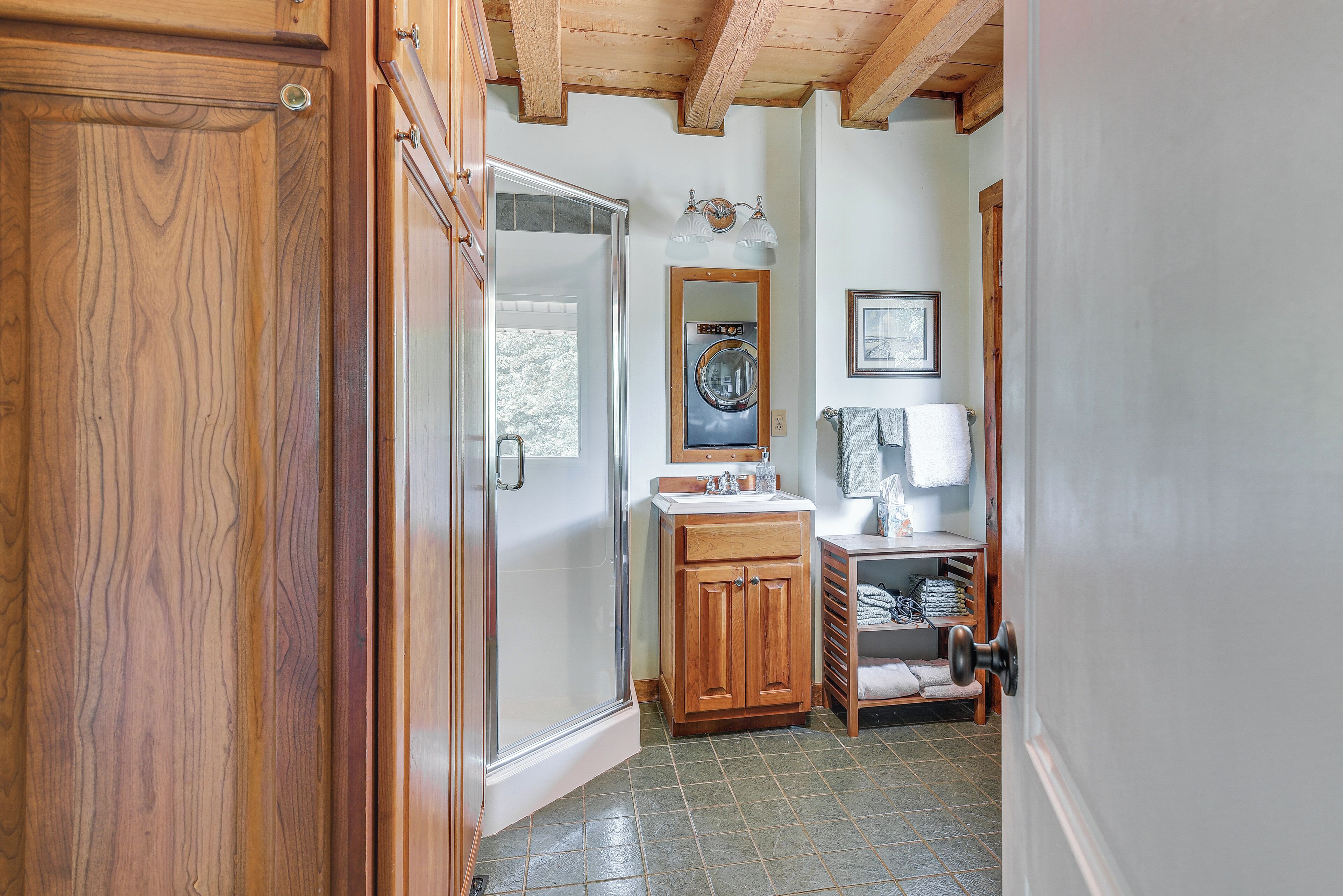 A bathroom with a wooden door, a glass shower door, a sink with a mirror, and a towel rack.