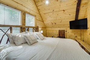 Un dormitorio de cabaña de madera con una cama, almohadas, un televisor y una ventana.