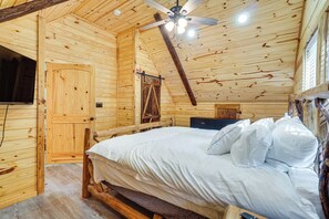 A wooden cabin interior with a bed, a ceiling fan, and a mounted television. - Cabin Retreat w/ Hot Tub Near Downtown Helen! (Helen)