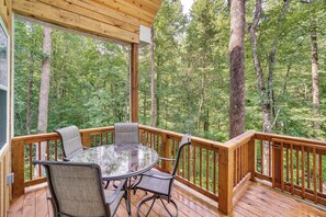 Une terrasse en bois avec une table et des chaises en verre, entourée d’une balustrade en bois, donnant sur une forêt.