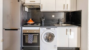 Una cuina compacta amb nevera, forn, rentadora, rentall i armaris.