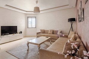 Uma sala de estar com sofá, mesa de centro, televisão e abajur.