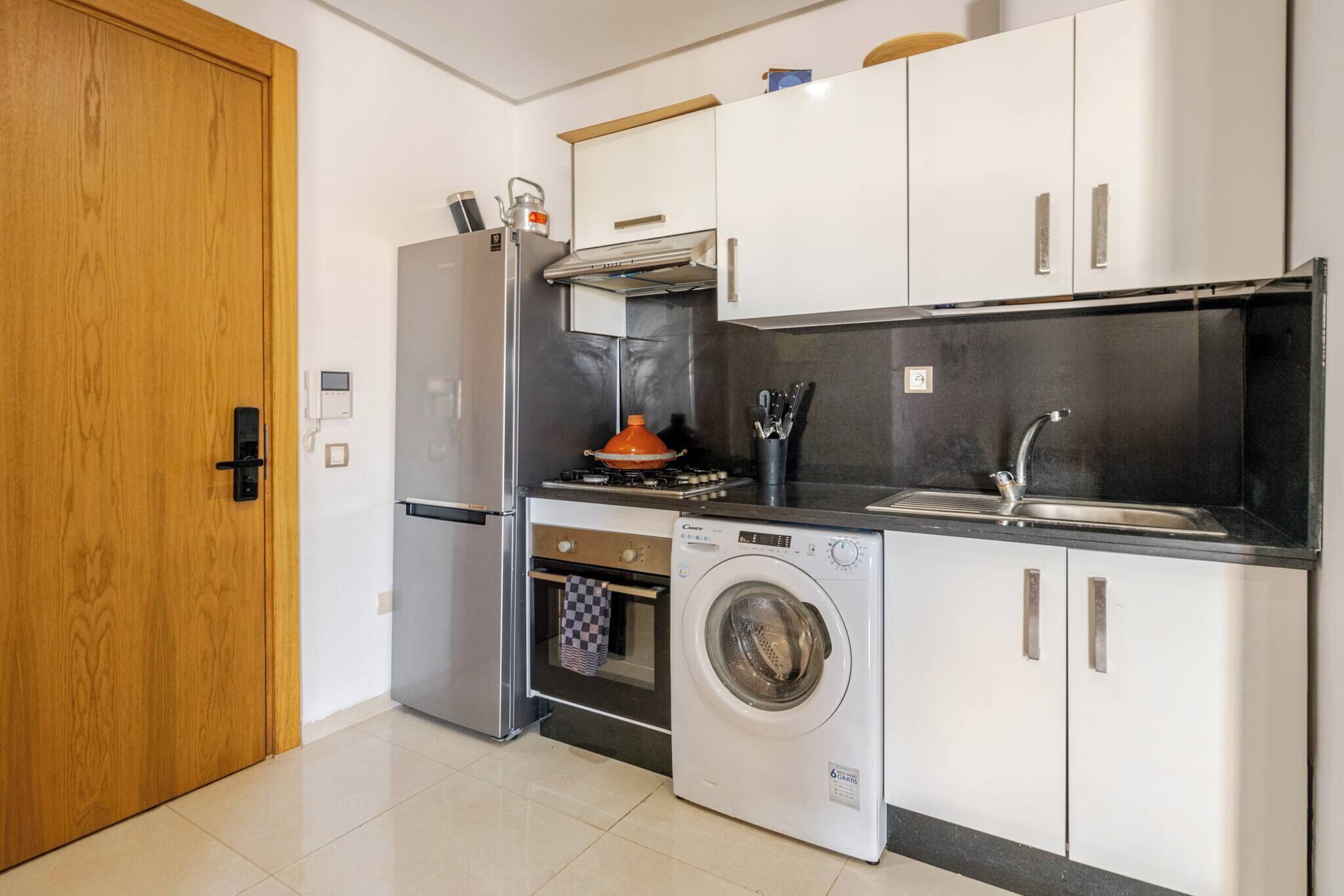 A compact kitchen with a refrigerator, oven, washing machine, and sink.