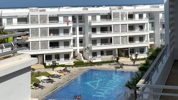 Un hotel modern amb diverses plantes, una piscina central, zones d'estar a l'aire lliure i vistes al mar.