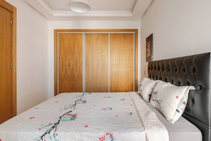 A bedroom with a bed, a headboard, a wardrobe, and a painting on the wall. - Beautiful apartment in Mansbay Beach next to the beach (Mansouria)