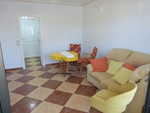 A living room with a checkered floor, a sofa, a chair, and a small table with a yellow tablecloth. - 1 bedroom apartment at 50 meters from the beach (Roquetas de Mar)