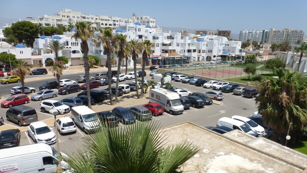 A parking lot with multiple cars and a few vans, surrounded by palm trees and buildings with white facades and blue domes. - 1 bedroom apartment at 50 meters from the beach (Roquetas de Mar)
