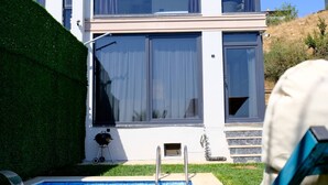 Una casa moderna con piscina, una parrilla y una silla bajo una sombrilla.