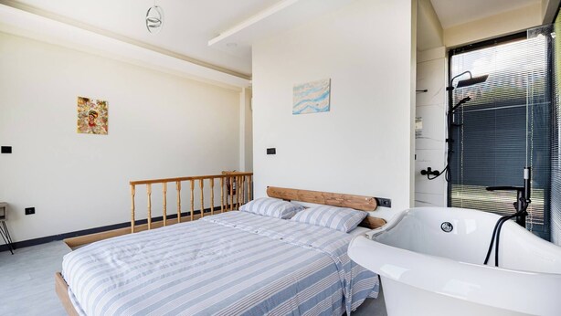 Un dormitorio moderno con una cama grande, cabecera de madera, bañera blanca y ventana con persianas.