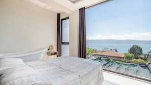 Un dormitorio con un ventanal grande, una cama y vista a un cuerpo de agua y un paisaje.