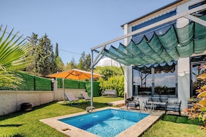 Un jardin avec une piscine, du mobilier d’extérieur et un patio couvert.