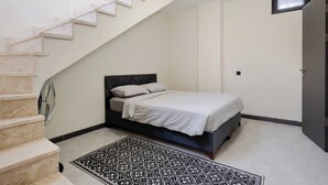 Un dormitorio con una cama, un tapete estampado, una escalera y una ventana pequeña.