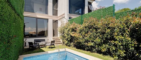 Une maison moderne dotée d’une piscine, de grandes fenêtres et d’un jardin bien entretenu.
