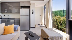 A modern room with a sofa, a bed, a small table, a kitchen area, and a large window with a view of greenery. - 2 Superior Villa Isıtmalı Havuz ve Deniz Manzara (Dilovası)