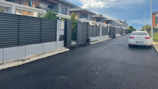 Una calle residencial moderna con casas, un coche blanco y cielo despejado.