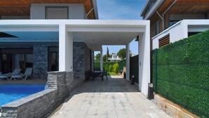 Una casa moderna con piscina, mobiliario exterior y una terraza cubierta.