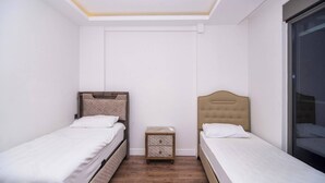 Un dormitorio pequeño y moderno con dos camas individuales, una mesita de noche y una ventana.
