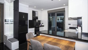 Una cocina moderna con un refrigerador negro, armarios blancos y una mesa de comedor de madera con sillas.