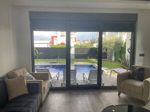 Una sala de estar con un amplio ventanal corredera que da a un área de piscina exterior.
