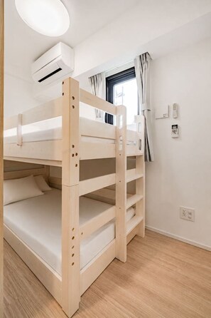 Ein Schlafraum mit Etagenbett, Fenster, Vorhängen, Klimaanlage und einer Wandsteckdose.