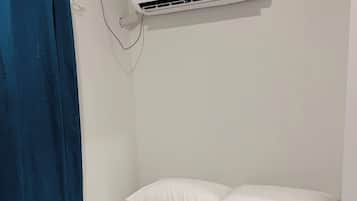 A single bed with white bedding, a blue curtain, and a wall-mounted air conditioning unit.