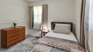 A bedroom with a wooden dresser, a bed with patterned bedding, a nightstand with a lamp, and a window with curtains. - Easy Trip to DC! Maryland Home w/ Great Location (Upper Marlboro)