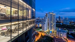 Un hotel moderno con fachada de vidrio, un bar en la azotea con asientos y vistas a la ciudad.