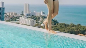 Una persona de pie junto a una piscina, con un paisaje urbano al fondo.