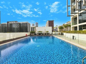 Una piscina sul tetto con cielo azzurro limpido, edifici moderni e poltrone prendisole.