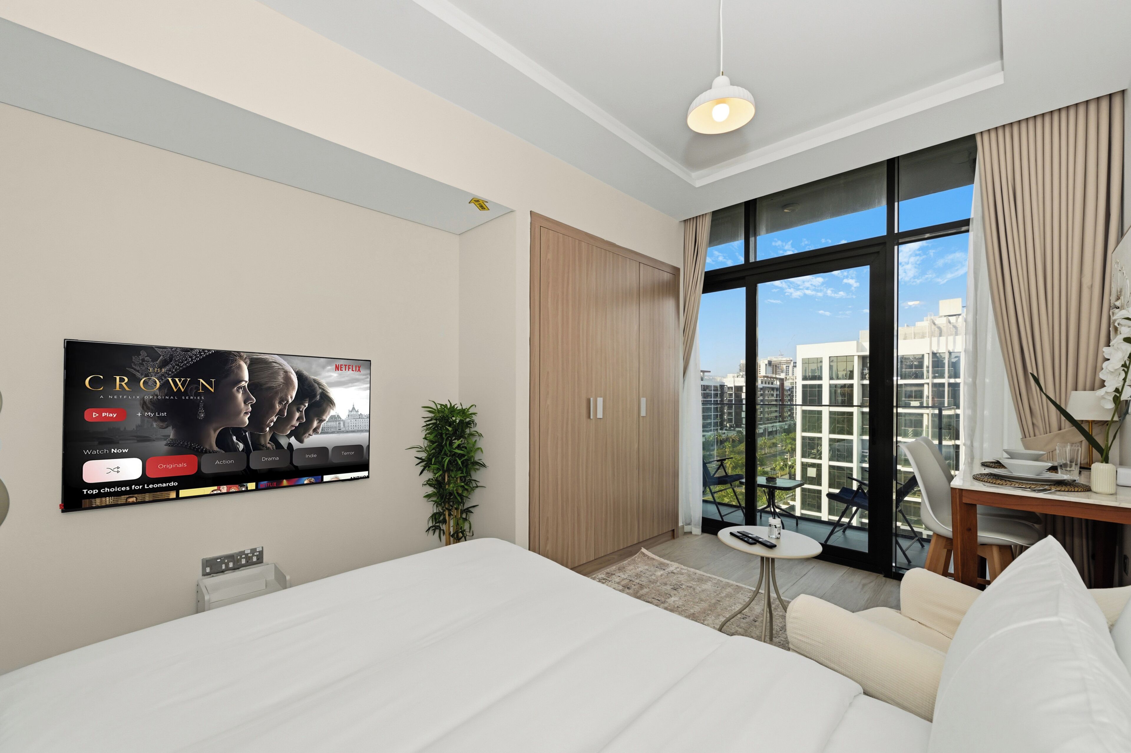 Ein modernes Hotelzimmer mit einem großen Bett, einem Schreibtisch mit Computer, einem an der Wand befestigten Fernseher und Blick auf die Stadt durch große Fenster.