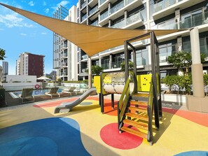 Ein Spielplatz mit Rutsche, Klettergerüst und bunten Fallschutzmatten.