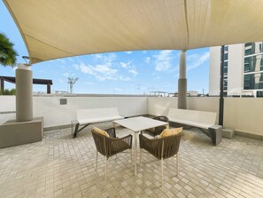 Ein möblierter Außenbereich mit Tisch und Stühlen, einem großen Sonnenschirm und Blick auf die Skyline der Stadt.