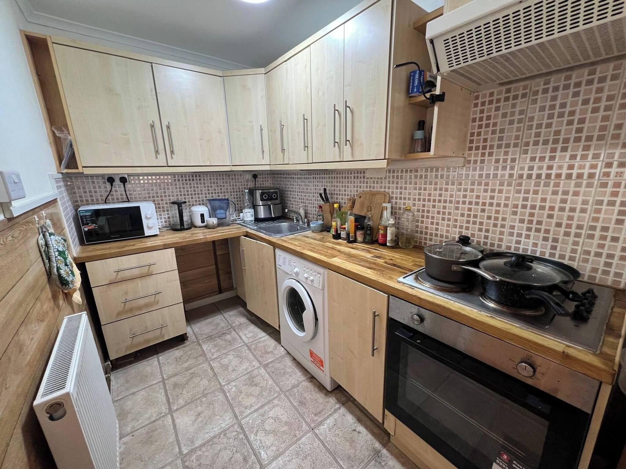 A compact kitchen with a microwave, toaster, washing machine, oven, and a small sink.