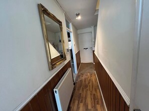 Ein schmaler Korridor mit Holzwandverkleidung, einem Heizkörper und einem großen Spiegel an der Wand.