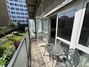 Ein Balkon mit Glastür, zwei Metallstühlen und einem kleinen Tisch.