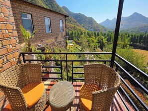 A stone building with two wicker chairs and a table on a balcony overlooking a mountainous landscape. - Clubhouse Resort Swarnagarh Udaipur (Udaipur)