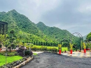 A paved driveway leading to a building with a view of lush green hills. - Clubhouse Resort Swarnagarh Udaipur (Udaipur)