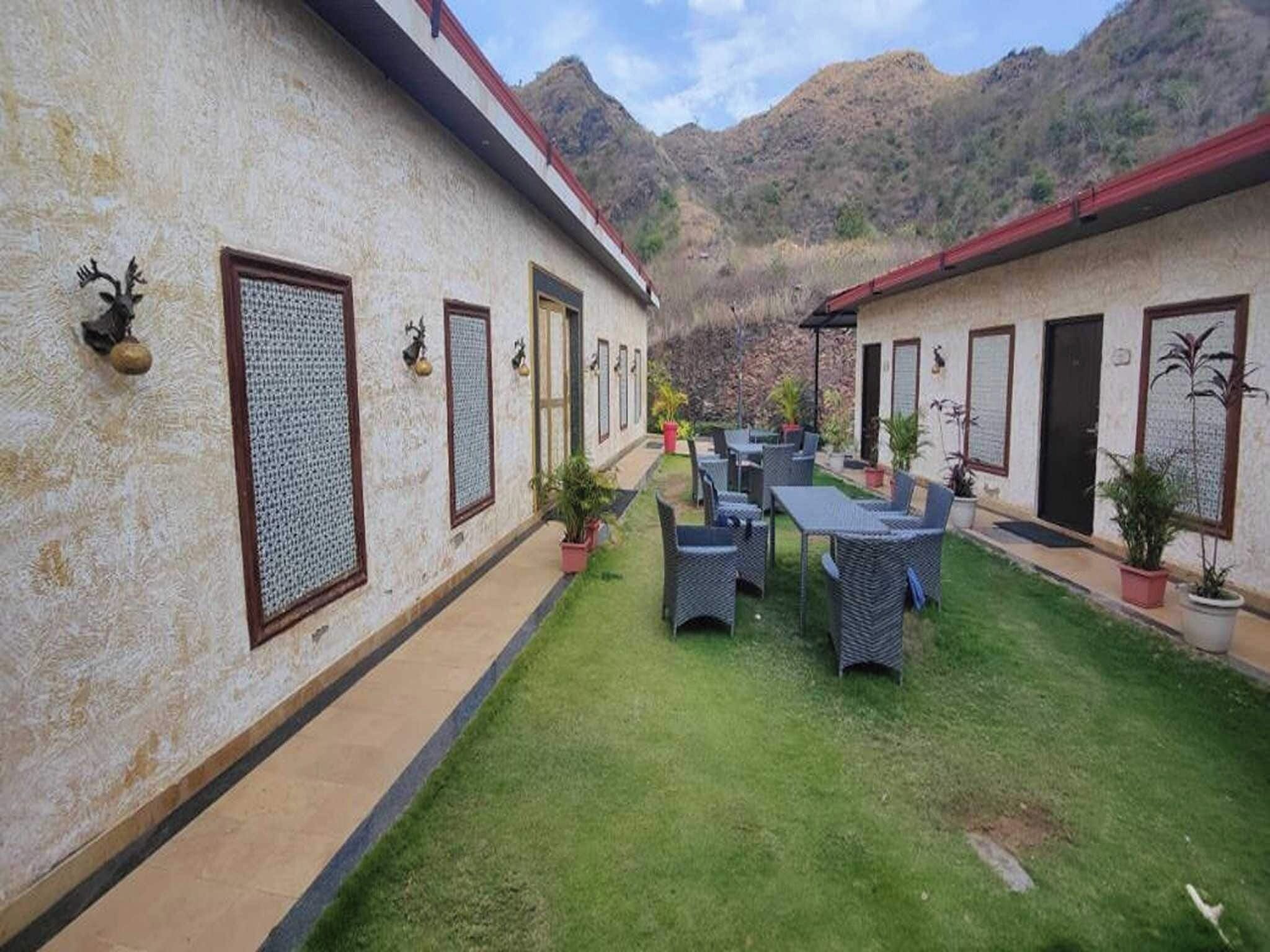 A courtyard with a dining area, two-story buildings, and a mountainous backdrop.