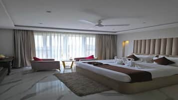 A hotel room with a large bed, a desk, a chair, a ceiling fan, and a view of the outside.