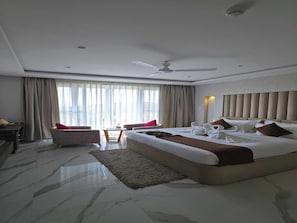 A hotel room with a large bed, a desk, a chair, a ceiling fan, and a view of the outside.