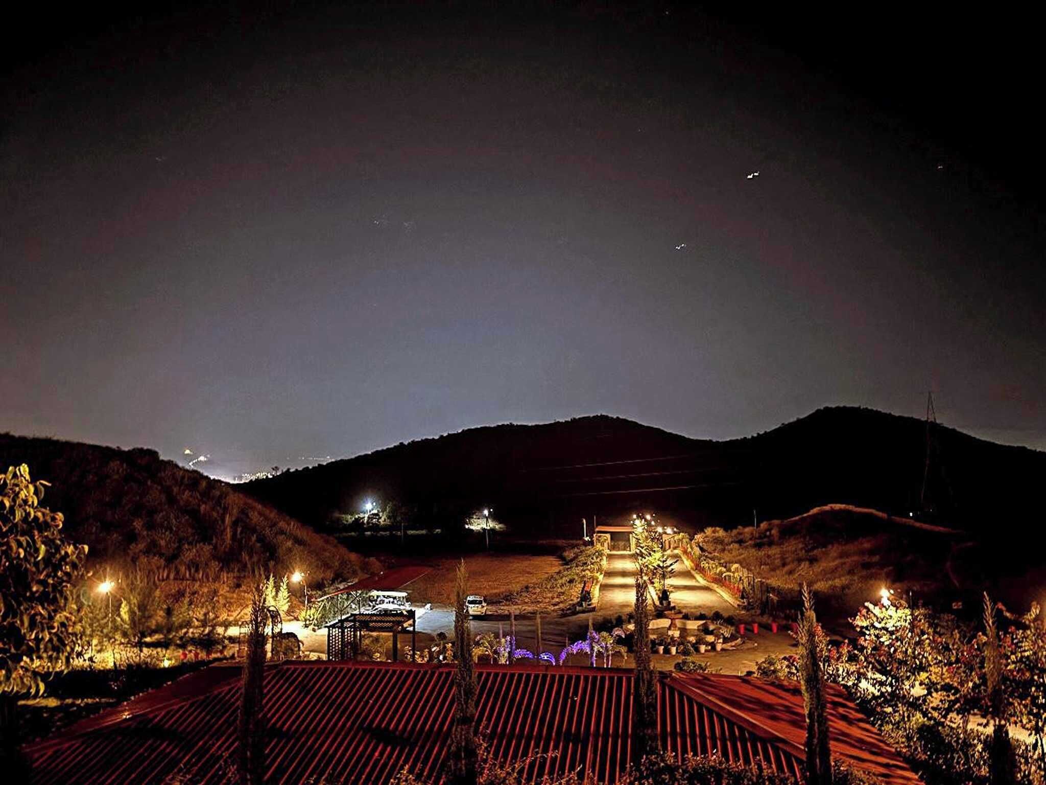 A nighttime view of a landscaped area with pathways, a gazebo, and distant lights on hills.