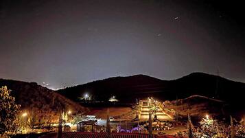 A nighttime view of a landscaped area with pathways, a gazebo, and distant lights on hills.