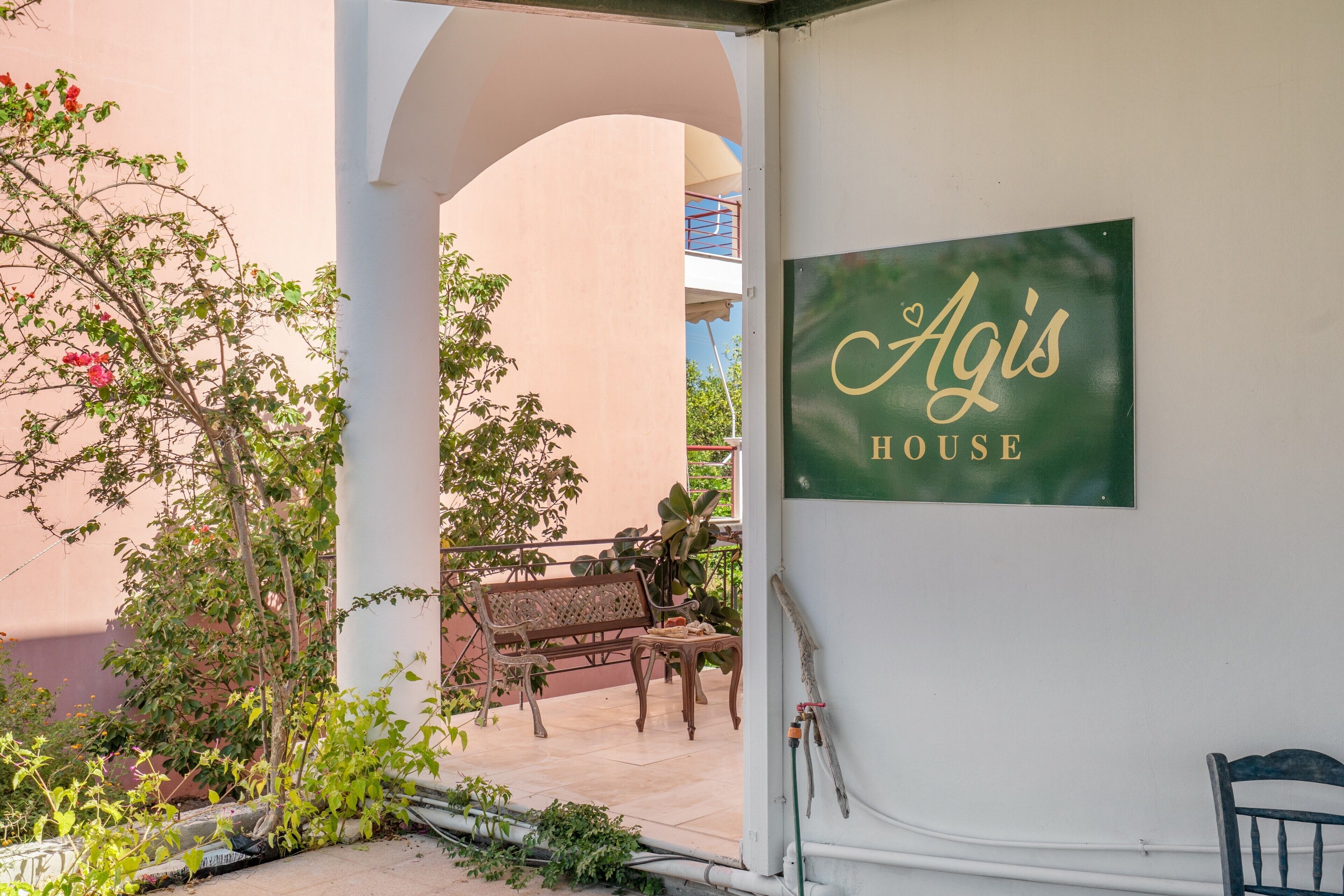A sign for 'Agis House' with a view of a courtyard featuring a bench and potted plants.