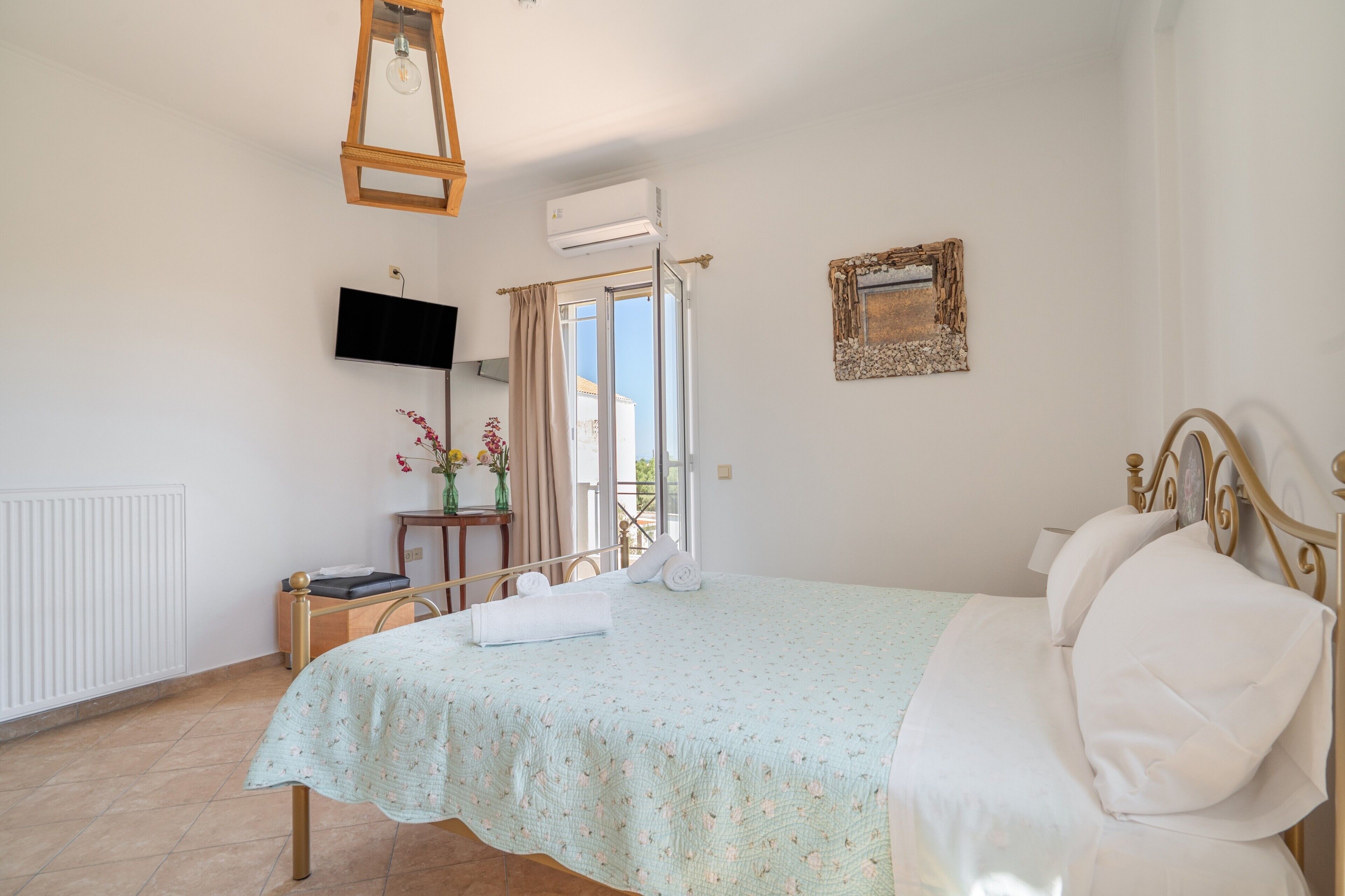 A bedroom with a bed, a television, a window with curtains, and a wall-mounted picture frame.
